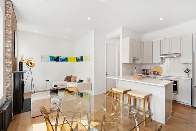 kitchen with tasteful backsplash, light wood-type flooring, appliances with stainless steel finishes, a kitchen breakfast bar, and radiator heating unit