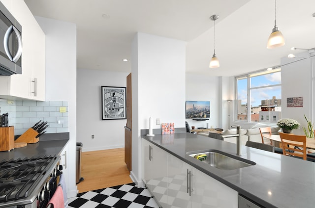 kitchen featuring sink, white cabinetry, backsplash, stainless steel appliances, and decorative light fixtures