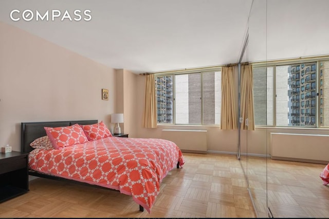 bedroom with multiple windows, light parquet flooring, and radiator heating unit