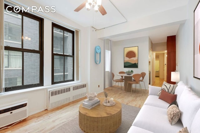 living room with radiator, light hardwood / wood-style floors, an AC wall unit, and ceiling fan