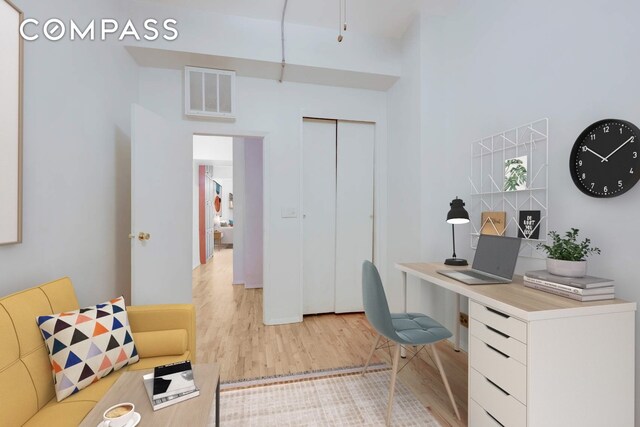 office area featuring visible vents, light wood-type flooring, and a towering ceiling