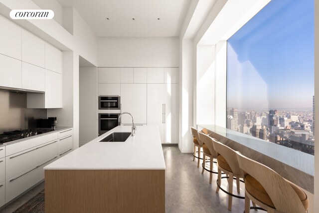 kitchen with white cabinetry, an island with sink, sink, and stainless steel gas cooktop