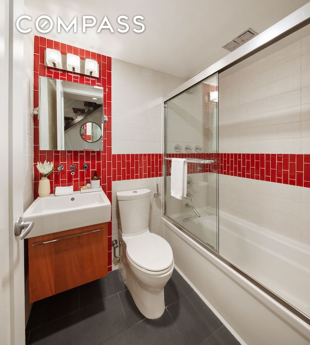 bathroom featuring tile patterned floors, visible vents, tile walls, bath / shower combo with glass door, and vanity