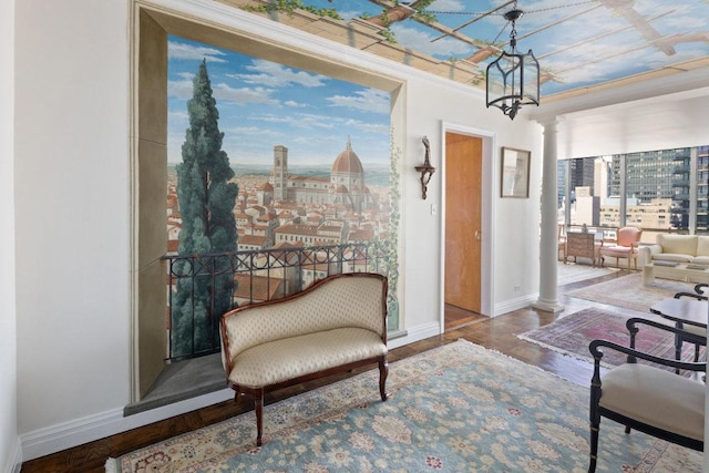 living area featuring hardwood / wood-style flooring, crown molding, an inviting chandelier, and decorative columns