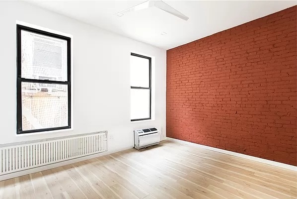 unfurnished room featuring heating unit, light wood-type flooring, radiator heating unit, ceiling fan, and brick wall