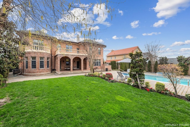 back of property featuring a fenced in pool, brick siding, a patio, a lawn, and a balcony