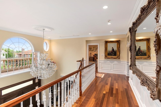 corridor with wood finished floors, crown molding, an upstairs landing, a decorative wall, and a notable chandelier