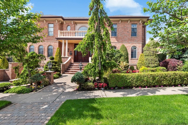 view of front of house featuring brick siding, a balcony, and a front lawn