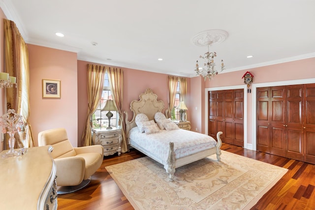 bedroom with crown molding, an inviting chandelier, wood finished floors, and multiple closets