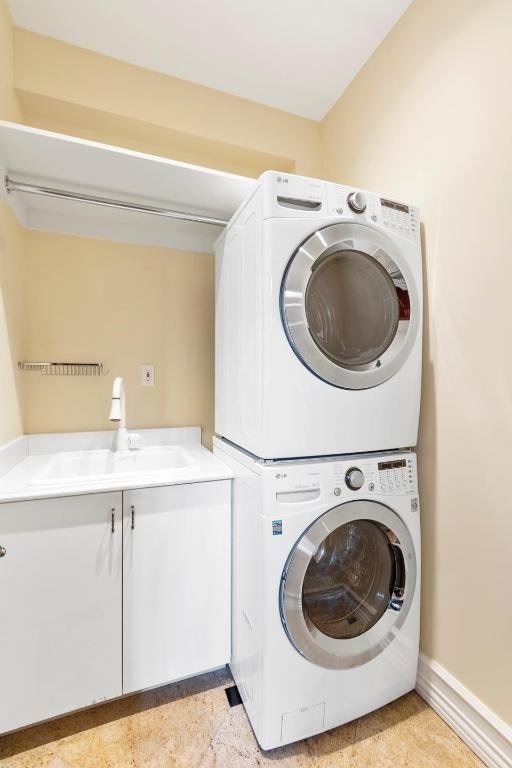 laundry area featuring cabinets, stacked washing maching and dryer, and sink