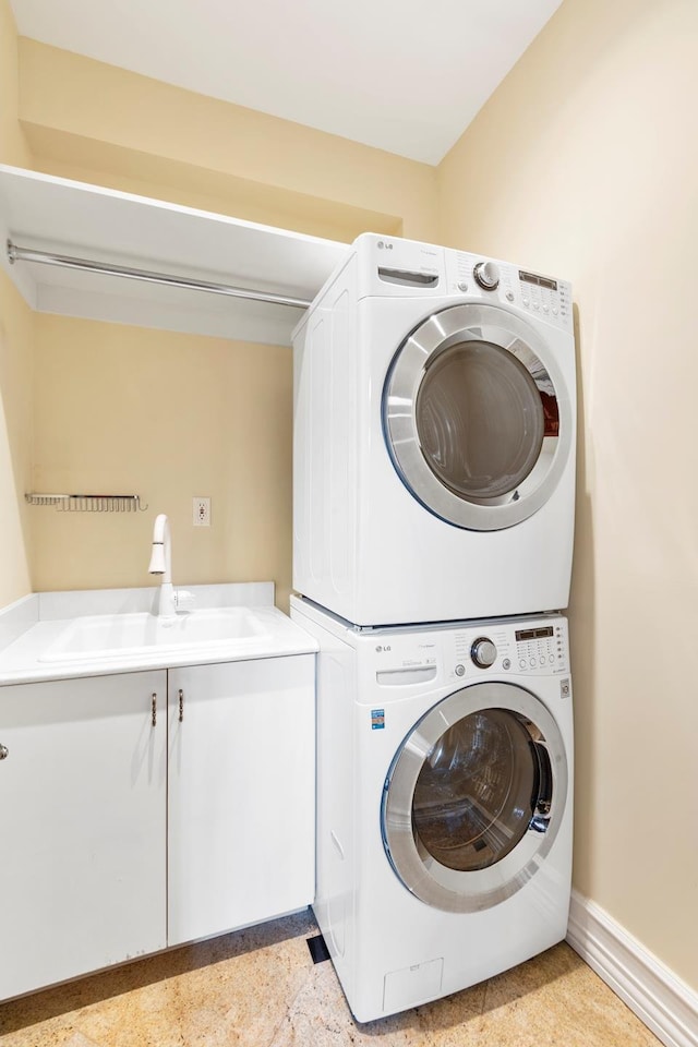 washroom with a sink, cabinet space, baseboards, and stacked washer / dryer