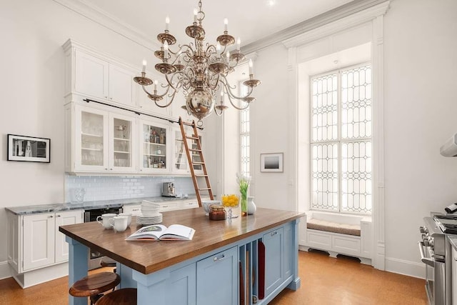 kitchen with butcher block countertops, stainless steel stove, hanging light fixtures, a notable chandelier, and white cabinets