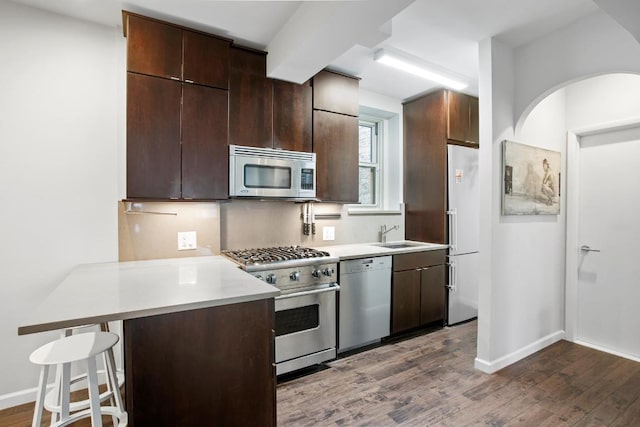 kitchen with a breakfast bar, sink, appliances with stainless steel finishes, dark hardwood / wood-style floors, and kitchen peninsula