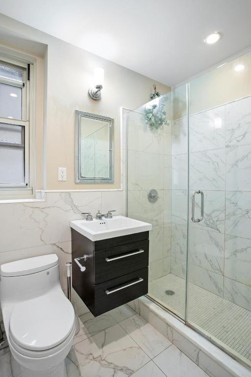 bathroom with vanity, a shower with shower door, tile walls, and toilet