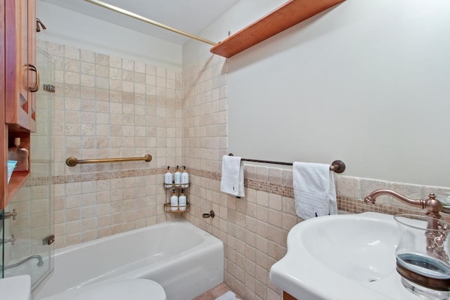 full bathroom featuring toilet, tiled shower / bath combo, sink, and tile walls