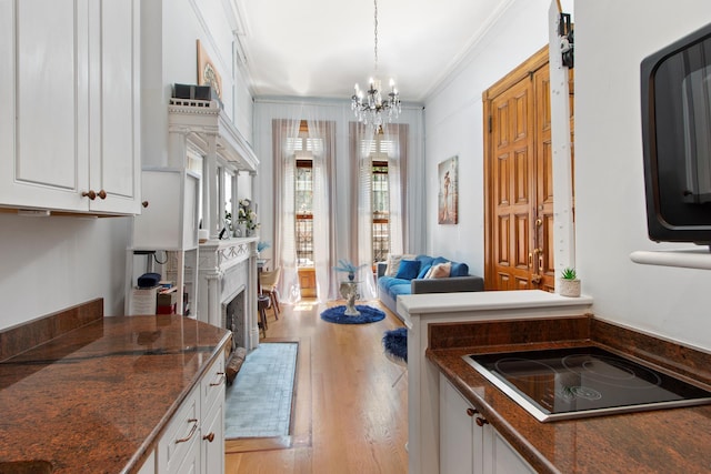 kitchen with black electric cooktop, dark countertops, a chandelier, white cabinetry, and light wood-style floors