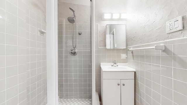 bathroom with vanity, tiled shower, and tile walls