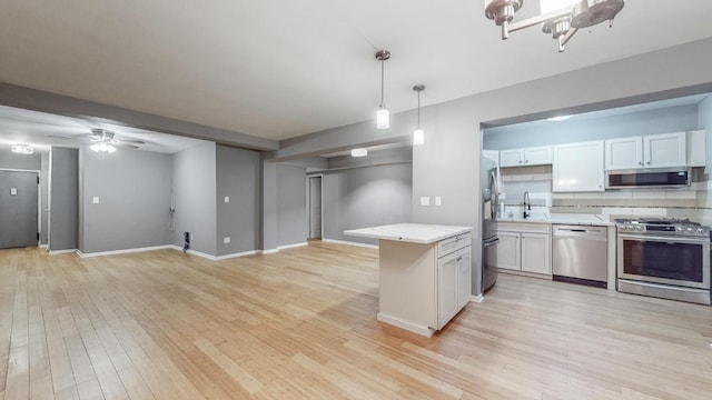 kitchen with sink, hanging light fixtures, stainless steel appliances, light hardwood / wood-style floors, and white cabinets