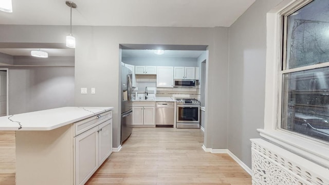 kitchen with appliances with stainless steel finishes, white cabinetry, hanging light fixtures, kitchen peninsula, and light wood-type flooring