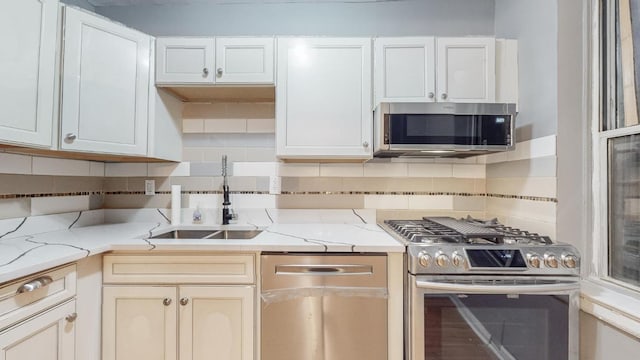 kitchen featuring sink, tasteful backsplash, white cabinetry, stainless steel appliances, and light stone countertops