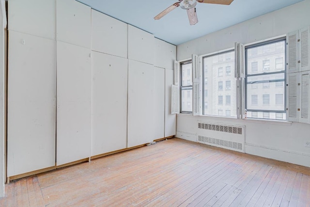 unfurnished bedroom featuring multiple windows, radiator heating unit, light hardwood / wood-style floors, and ceiling fan