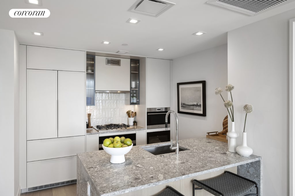 kitchen with stainless steel gas cooktop, sink, white cabinetry, kitchen peninsula, and backsplash