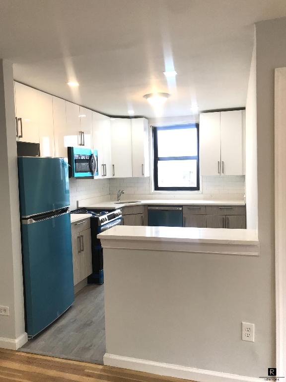 kitchen featuring tasteful backsplash, range, white cabinets, and refrigerator