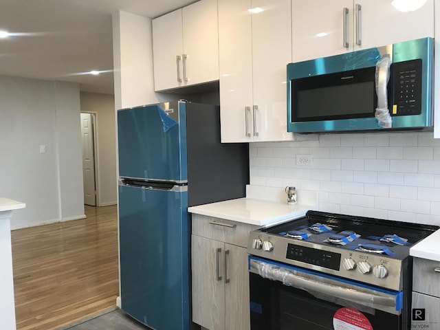 kitchen with stainless steel stove, refrigerator, white cabinetry, decorative backsplash, and hardwood / wood-style flooring