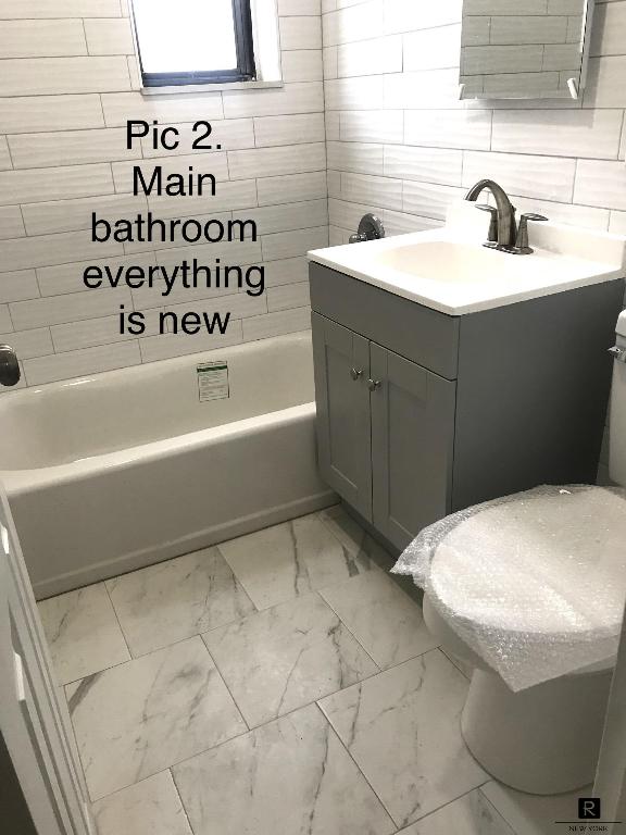 full bathroom featuring tiled shower / bath combo, vanity, tile walls, and toilet