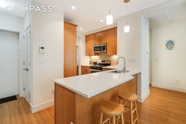 kitchen with backsplash, light wood-type flooring, brown cabinets, stainless steel appliances, and a sink