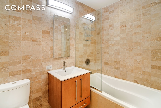 full bath featuring vanity, tile walls, toilet, and tiled shower / bath combo