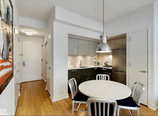 kitchen featuring pendant lighting, sink, light hardwood / wood-style flooring, stainless steel refrigerator, and backsplash