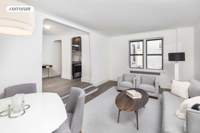 living room featuring arched walkways, wood finished floors, visible vents, and baseboards