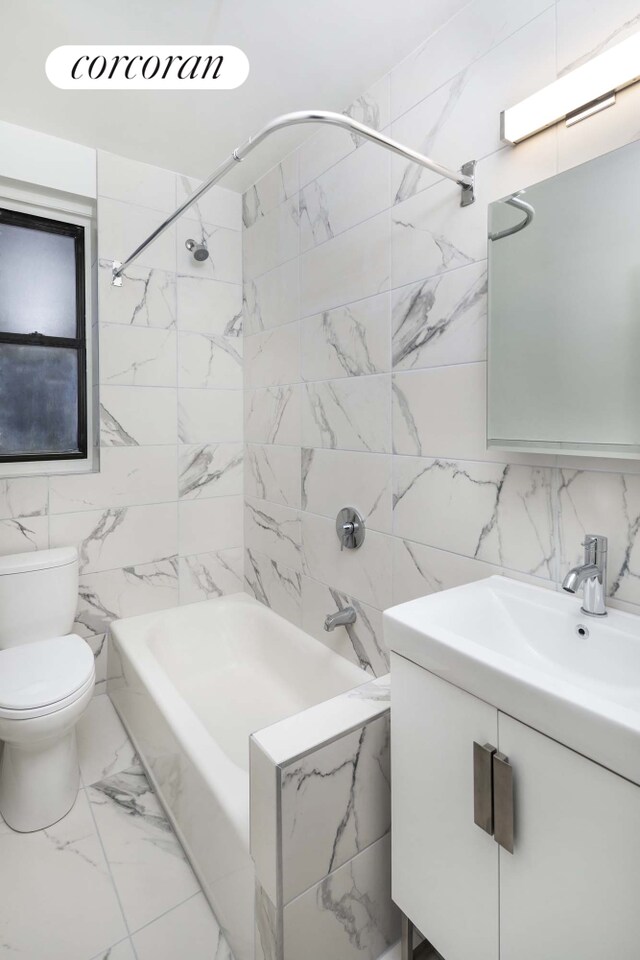 full bathroom with tiled shower / bath, tile walls, vanity, and toilet