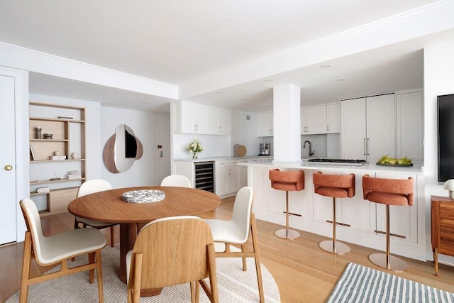 dining space featuring wine cooler, sink, and light wood-type flooring