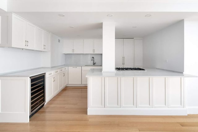 kitchen featuring sink, wine cooler, white cabinets, kitchen peninsula, and light wood-type flooring