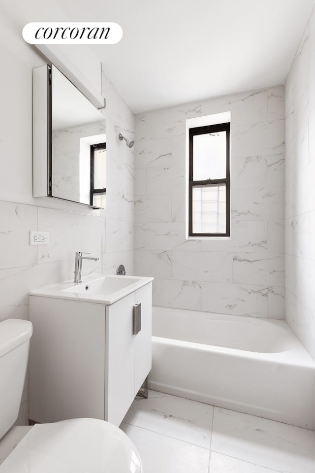 bathroom with toilet, vanity, tile walls, marble finish floor, and  shower combination