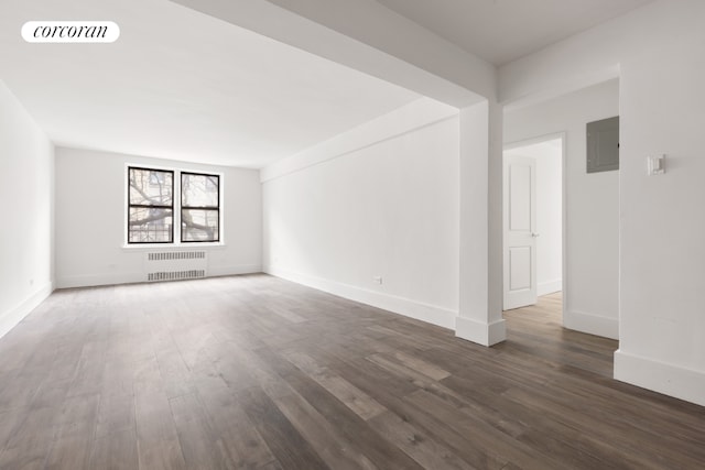 empty room with radiator heating unit, dark hardwood / wood-style floors, and electric panel