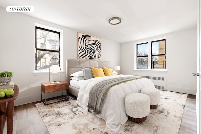 bedroom featuring multiple windows, radiator heating unit, and light wood-type flooring