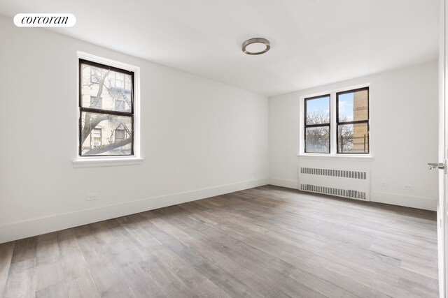 unfurnished room with plenty of natural light, radiator heating unit, and light wood-type flooring