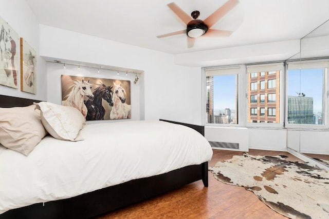 bedroom with hardwood / wood-style flooring, ceiling fan, radiator, and multiple windows