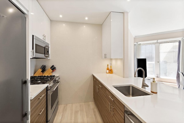 kitchen featuring dark brown cabinets, sink, white cabinetry, light hardwood / wood-style floors, and stainless steel appliances