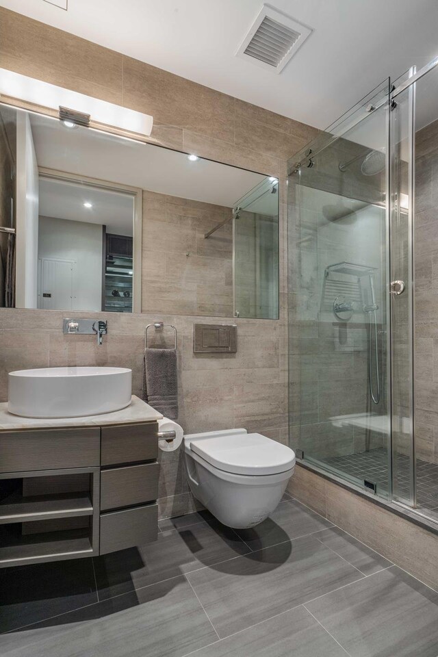 bathroom with vanity, toilet, tile walls, and a shower with shower door