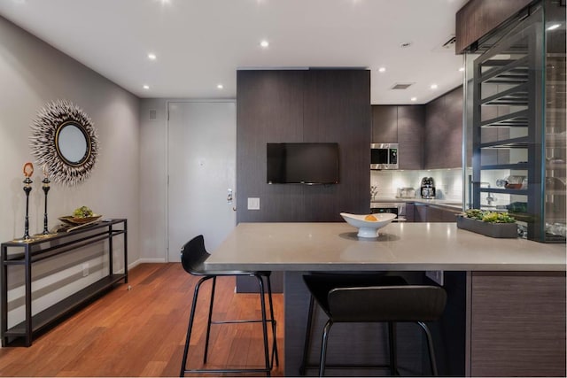 kitchen with tasteful backsplash, a breakfast bar area, kitchen peninsula, dark brown cabinets, and light hardwood / wood-style flooring