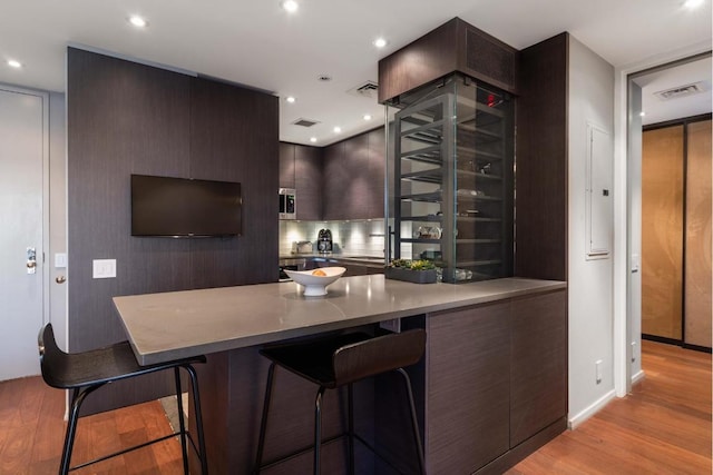 kitchen with a kitchen breakfast bar, dark brown cabinetry, kitchen peninsula, elevator, and light wood-type flooring