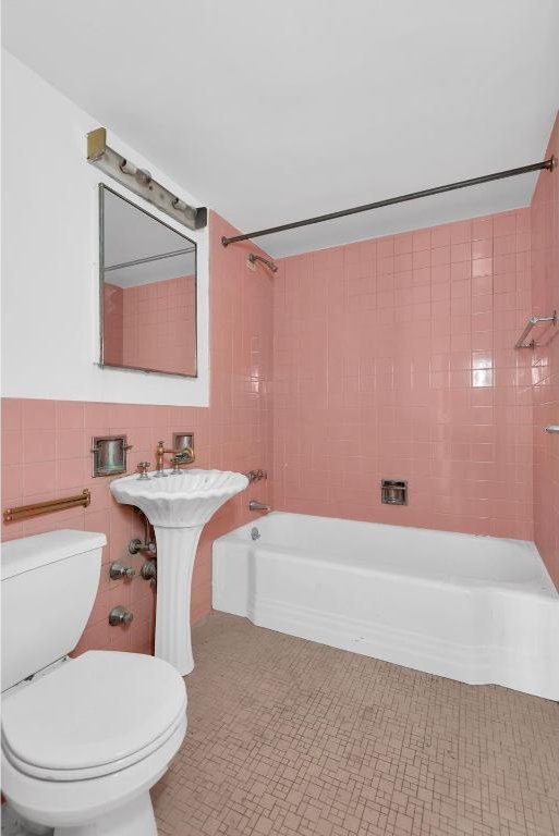 full bathroom featuring tiled shower / bath, toilet, sink, and tile walls