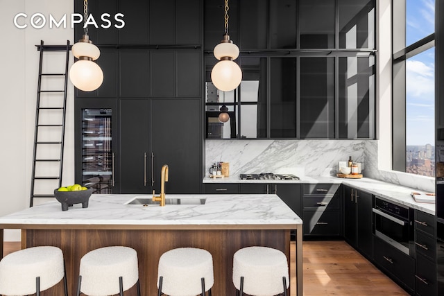 kitchen featuring dark cabinetry, beverage cooler, a kitchen breakfast bar, and a sink