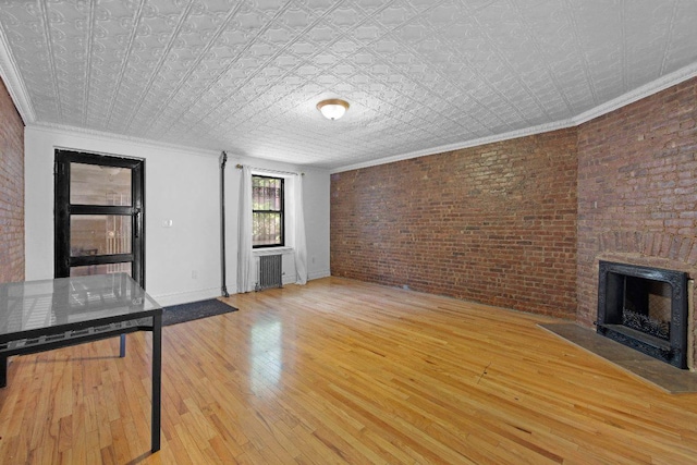 unfurnished living room with crown molding, brick wall, a brick fireplace, and light wood-type flooring