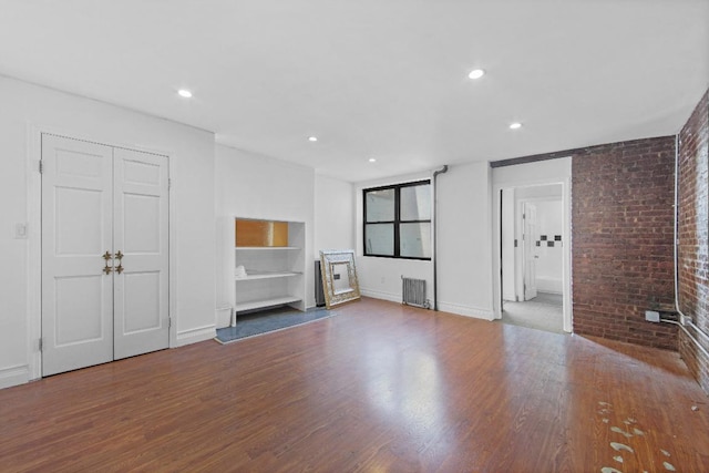 unfurnished living room featuring hardwood / wood-style floors, brick wall, and radiator heating unit