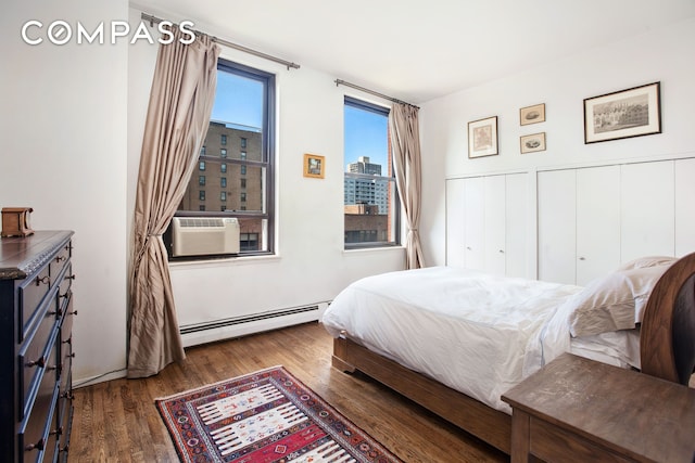 bedroom with a wainscoted wall, baseboard heating, cooling unit, wood finished floors, and a view of city